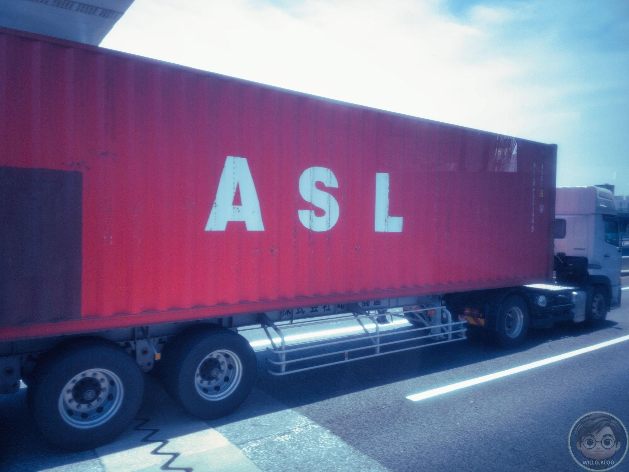 Midday light flattens everything—except that red ASL container cutting through the lane.